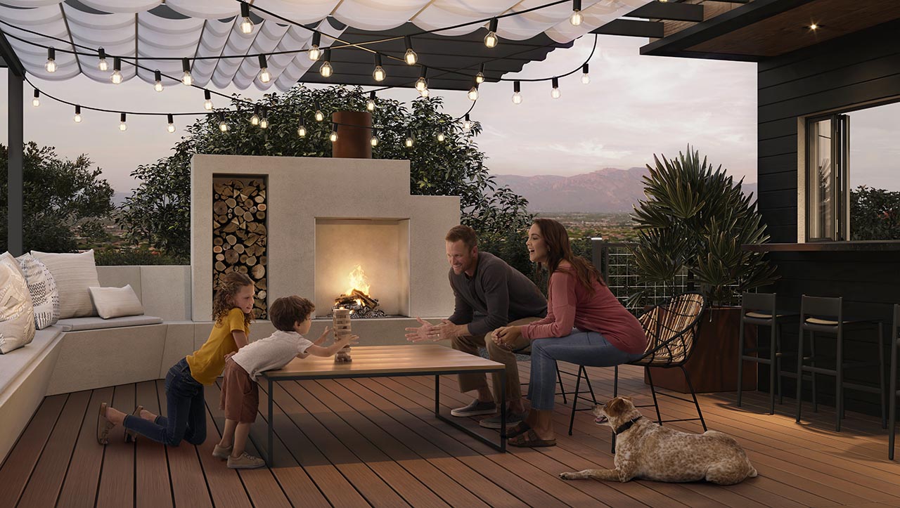 A family around table playing jenga next to a fire pit table on their deck, made of Trex Signature Ocracoke. It is night and lights are set up across the deck to create a warm and calming feeling. 